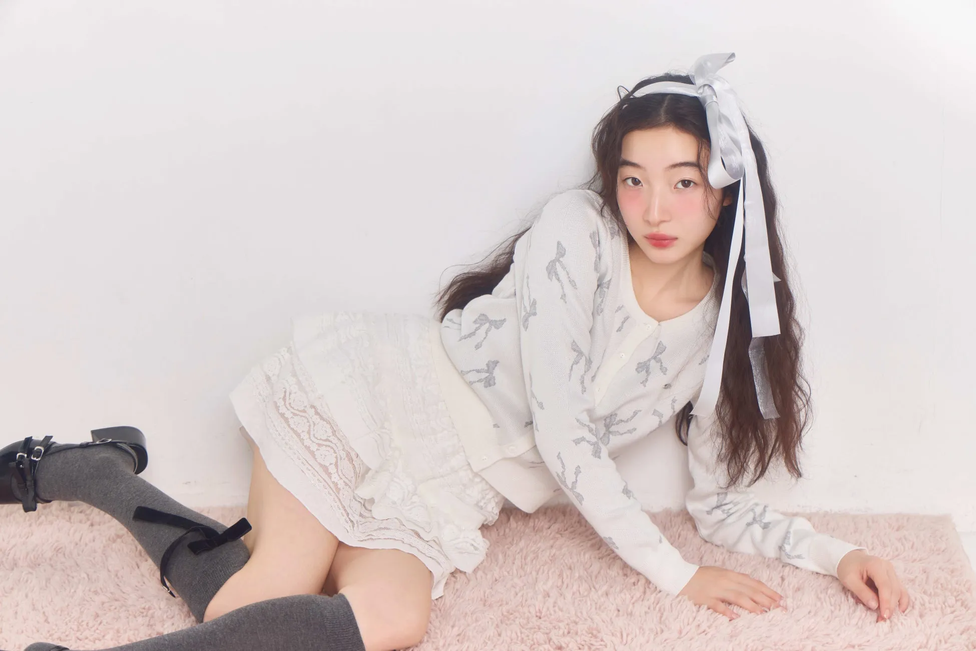 ピンクのカーペットの上に横たわる女性が着るリボンニットカーディガン