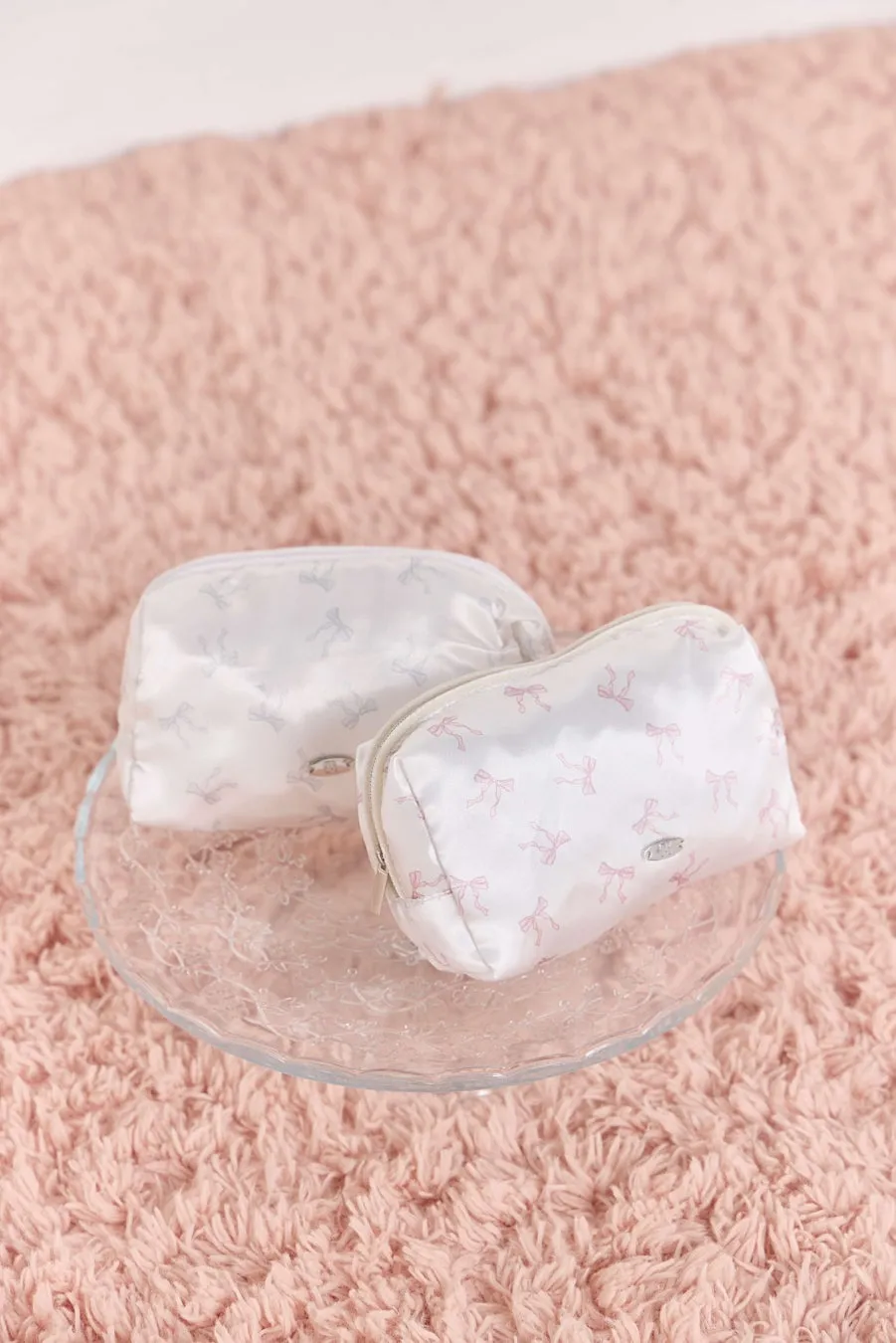 ピンク色のカーペットの上に置かれたリボン模様の白いポーチ