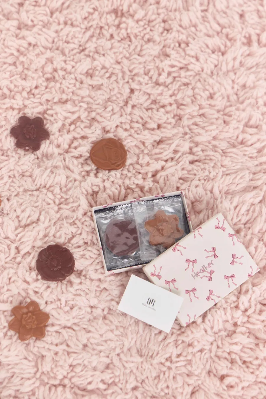 ピンクの毛布の上に、花やバラの形をしたチョコレートとリボン柄の箱
