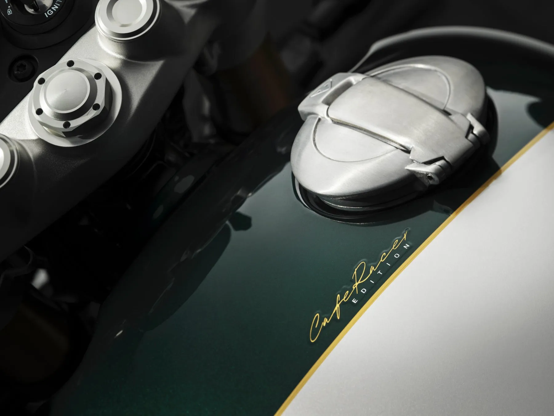 バイクの燃料タンクのクローズアップ写真。ダークグリーンとシルバーのツートンカラーで、"Cafe Racer Edition"の文字が金色で書かれています。