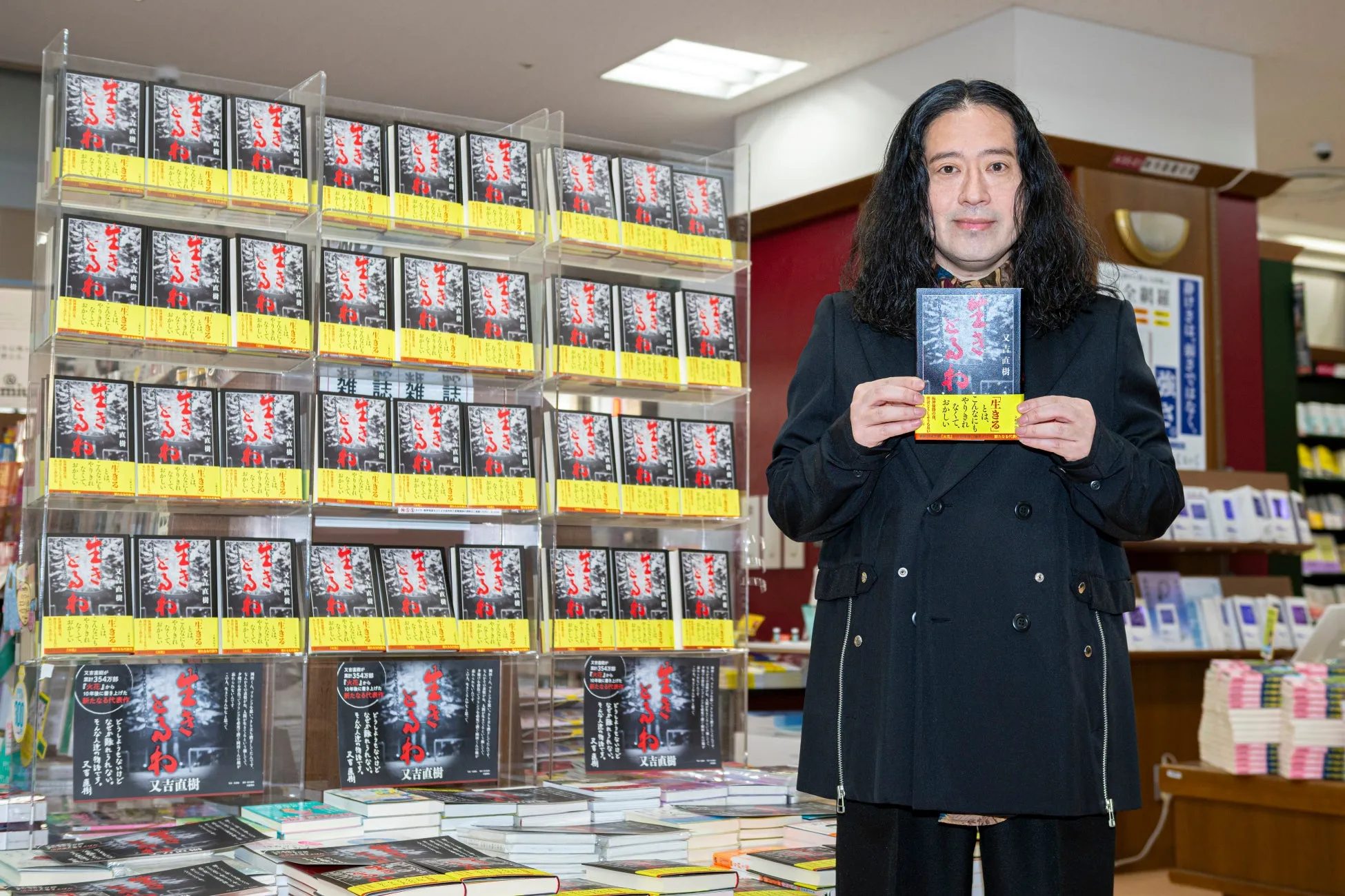 又吉直樹が自身の著書「生きる」を持って立っている写真