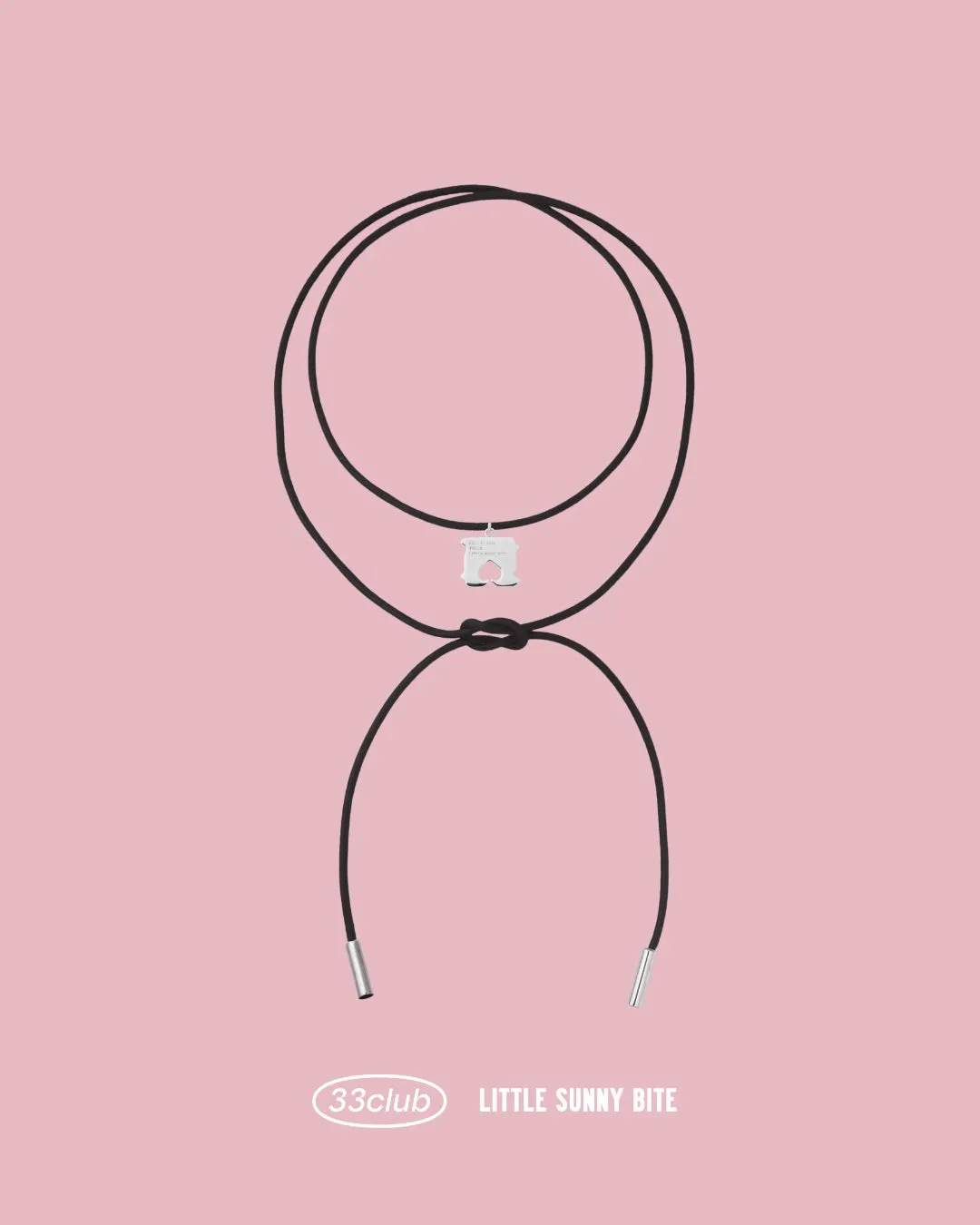 ピンクの背景に、白い犬の形をしたペンダントが付いた黒い紐のネックレス。