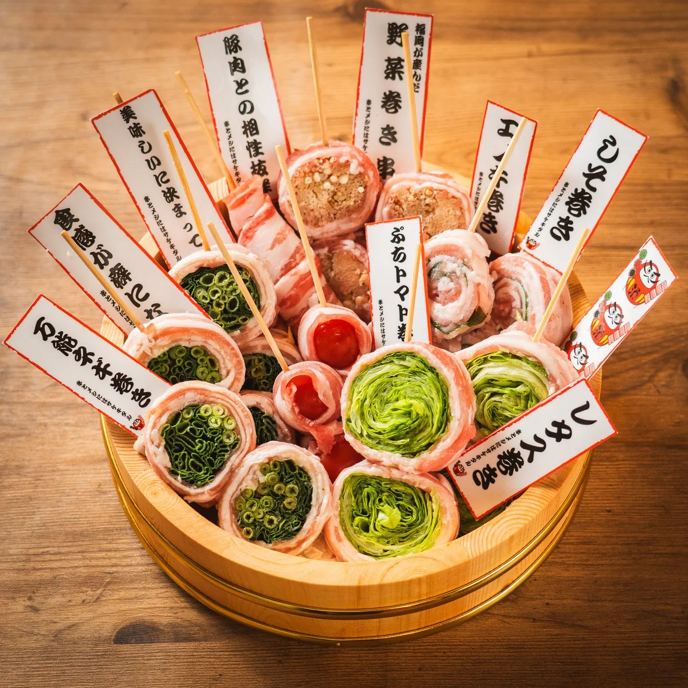 木製の桶に盛り付けられた、豚肉で巻かれた串料理の集合写真