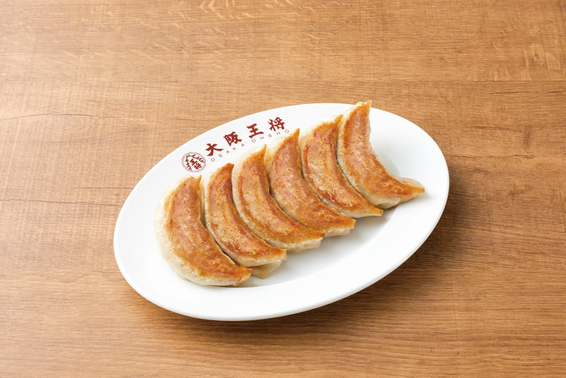 大阪王将の焼き餃子が白皿に盛り付けられた写真。木目のテーブルの上に置かれている。