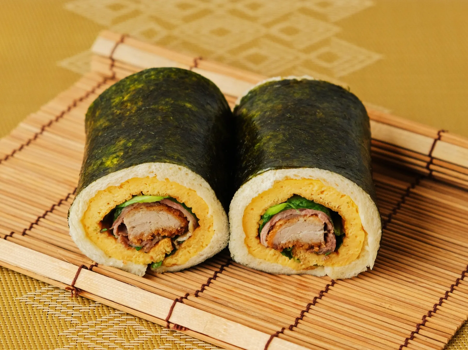 海苔で巻かれたサンドイッチ。断面には、卵焼き、肉、葉物野菜が見える。