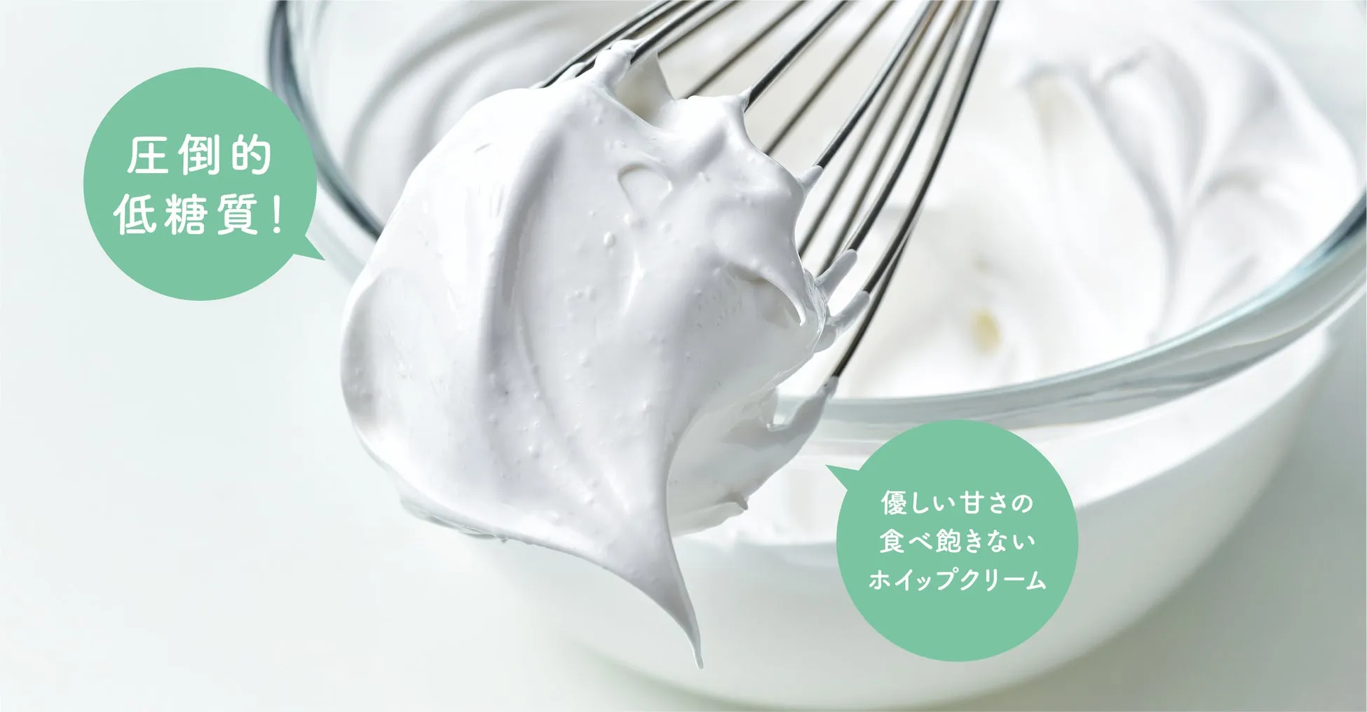 泡立て器で泡立てられたホイップクリームの写真。ホイップクリームは、ガラスのボウルに入れられており、泡立て器がクリームから突き出ている。背景は白く、ホイップクリームに焦点を当てている。