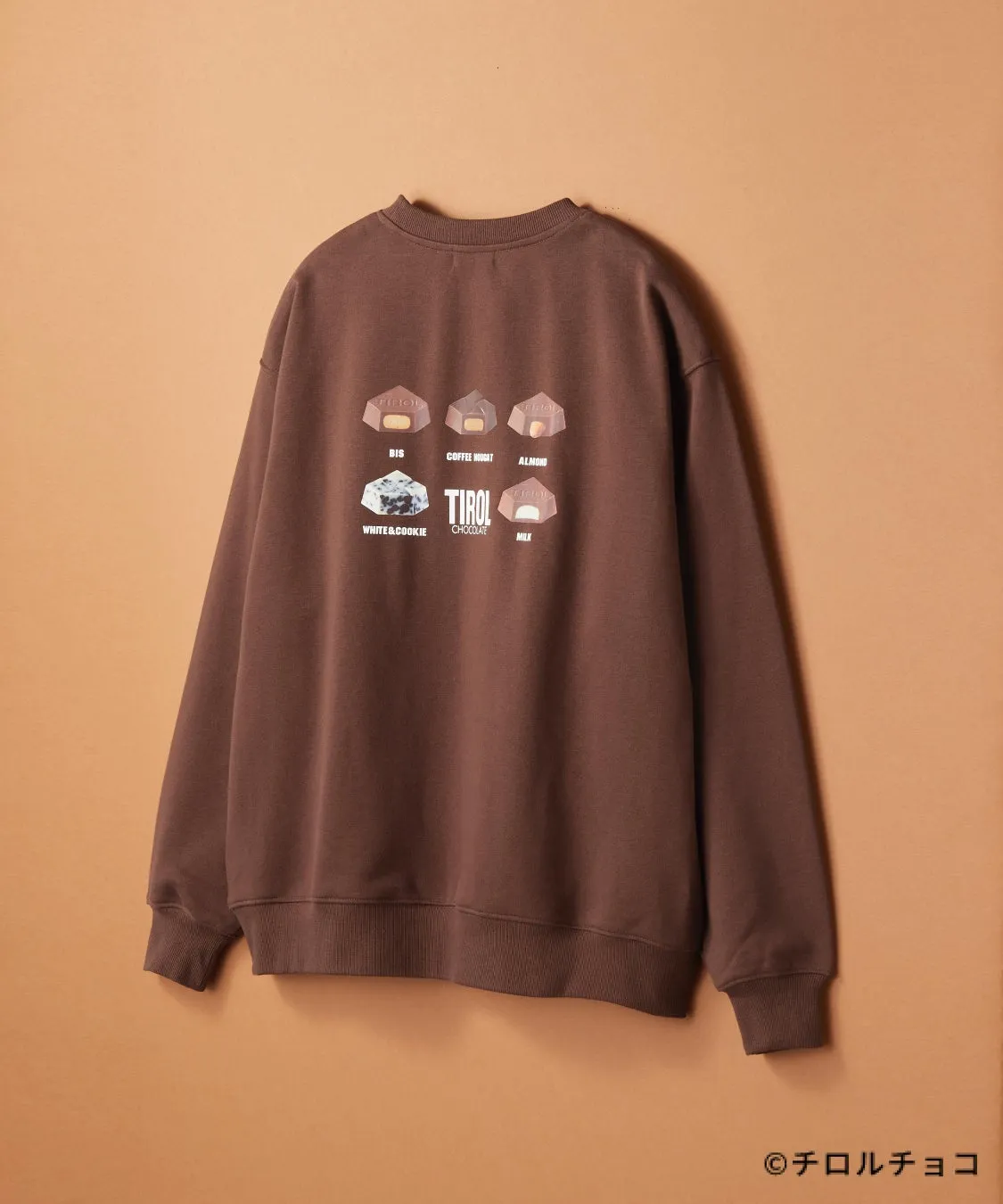 茶色のトレーナーにチロルチョコのイラストがプリントされた画像です。トレーナーには、BIS、COFFEE NOUGAT、ALMOND、WHITE&COOKIE、TIROL CHOCOLATE、MILKの文字とイラストが描かれています。下部には©チロルチョコの文字があります。