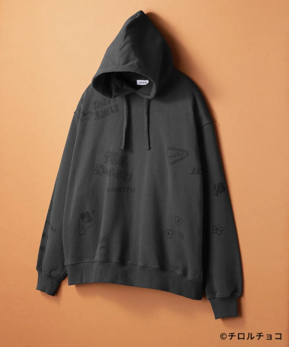 黒色のパーカーに「HAPPY SMILE」や「TIROL CHOCOLATE」の文字、花のイラストなどが描かれています。右下には「©チロルチョコ」の文字があります。