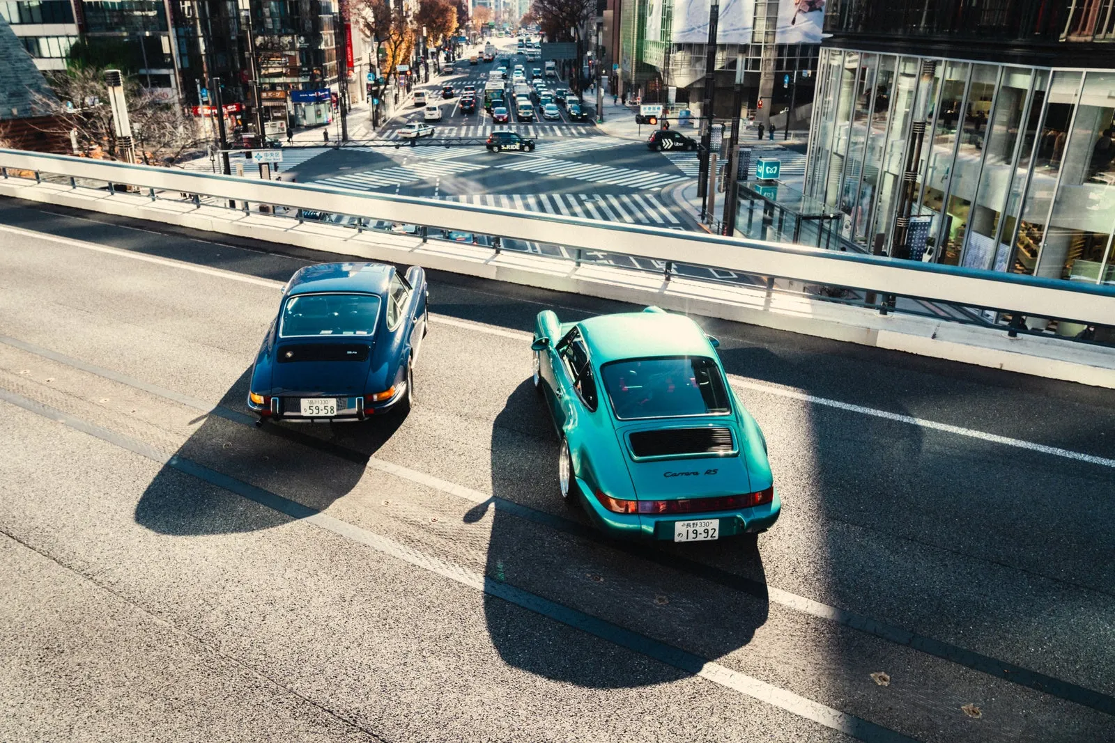 2台のポルシェが道路を走行している様子を捉えた写真です。奥には都市の景色が広がっています。