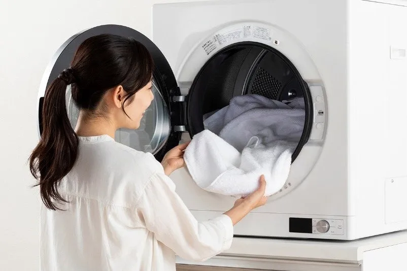 女性が洗濯機にタオルを入れている様子。