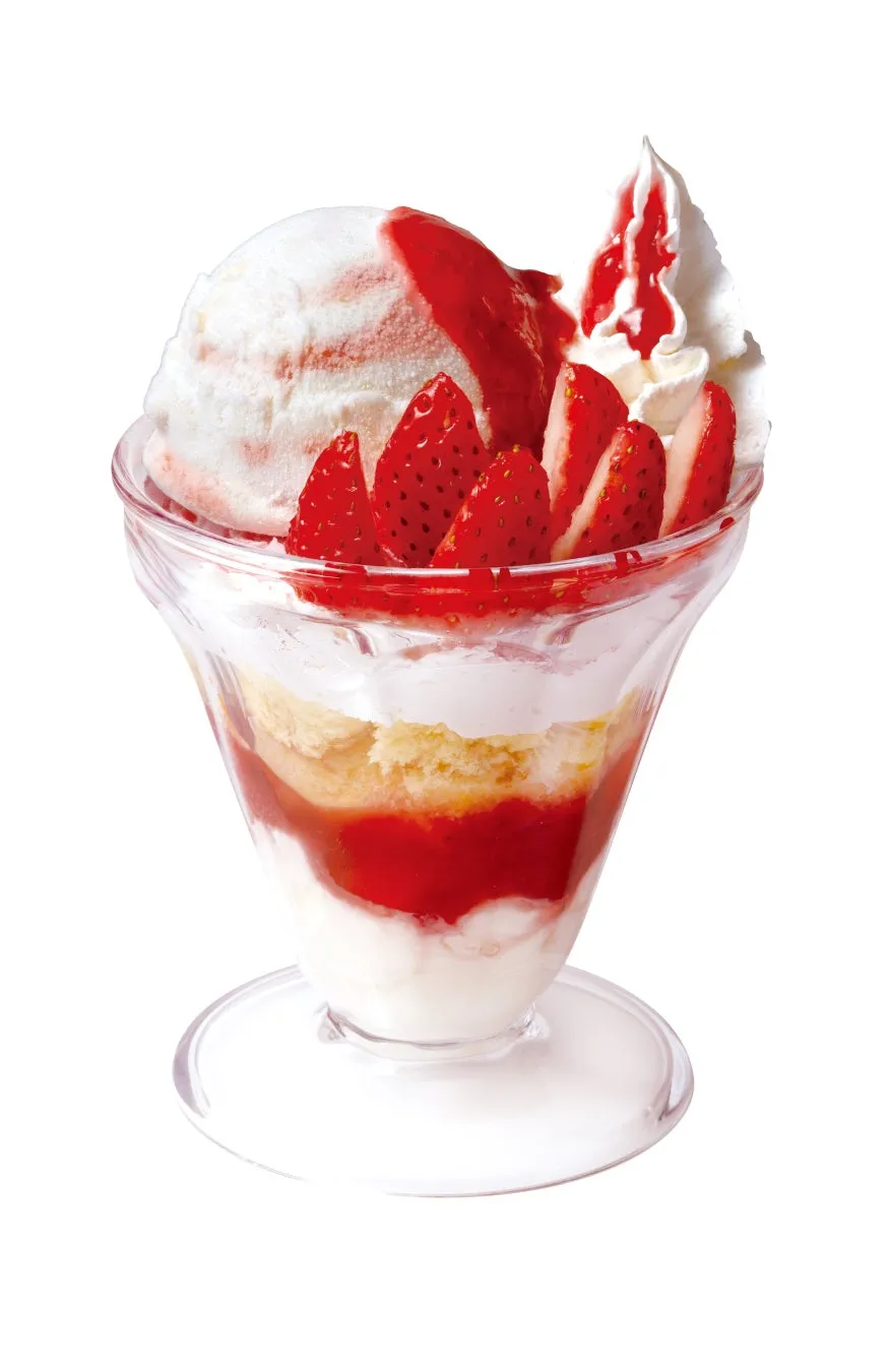 透明なグラスに入ったイチゴパフェ。上にはアイスクリーム、イチゴのスライス、ホイップクリームがトッピングされている。