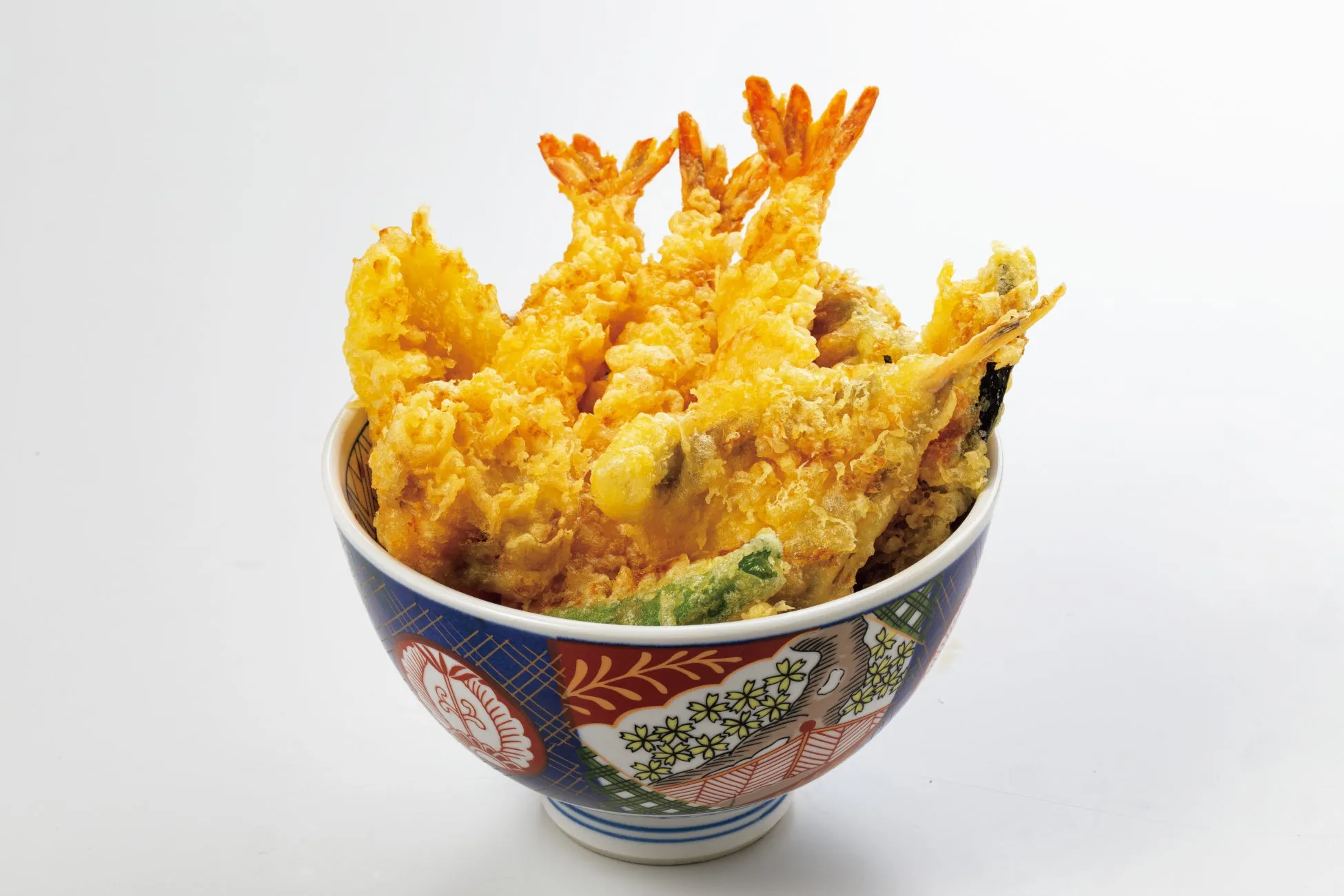 天ぷらが盛られた丼の画像です。エビの天ぷらがメインで、その他にも野菜の天ぷらが入っています。丼は鮮やかな柄で彩られています。