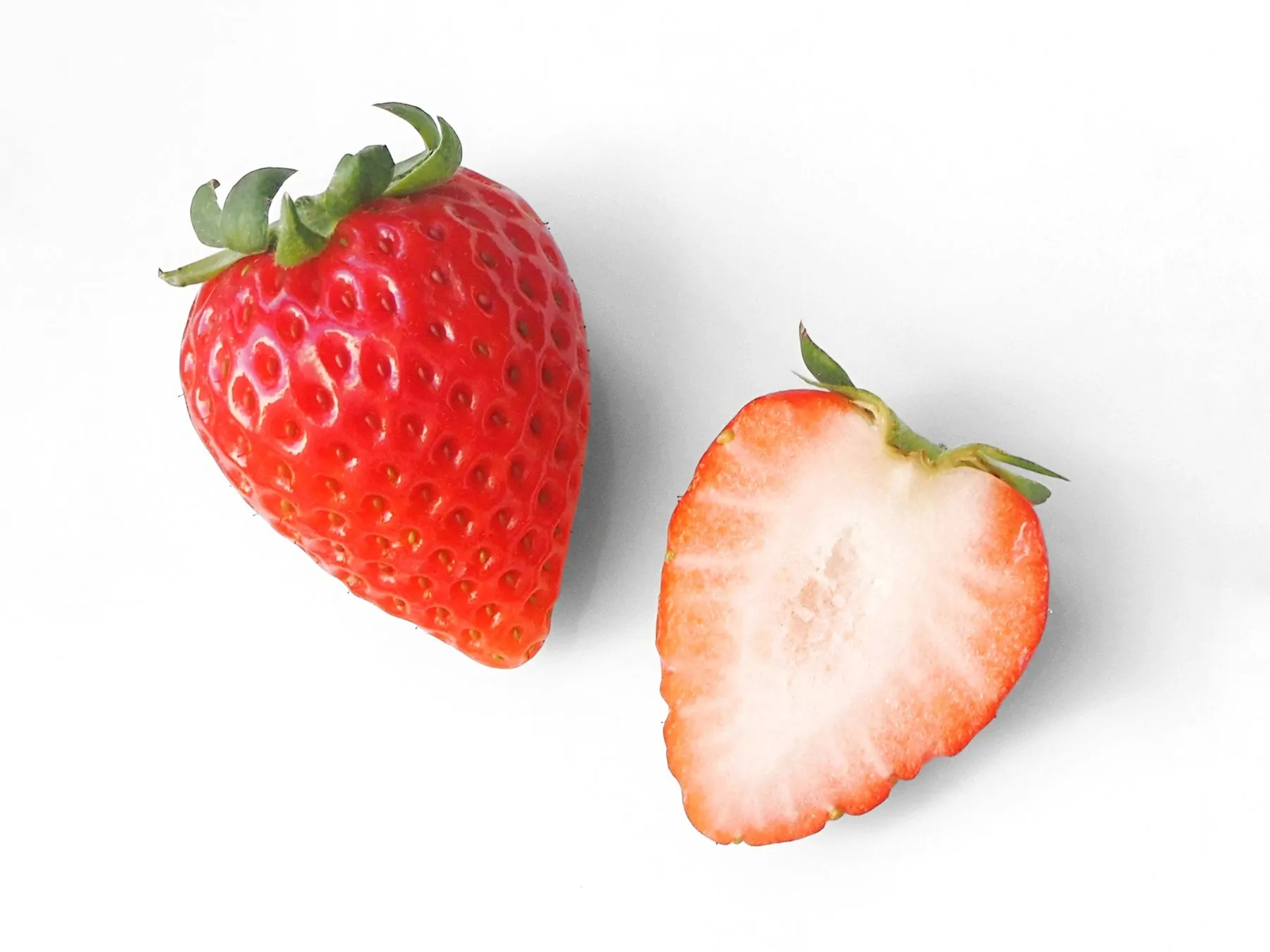 2つのイチゴが白い背景に配置された写真です。一つは丸ごと、もう一つは半分にカットされています。