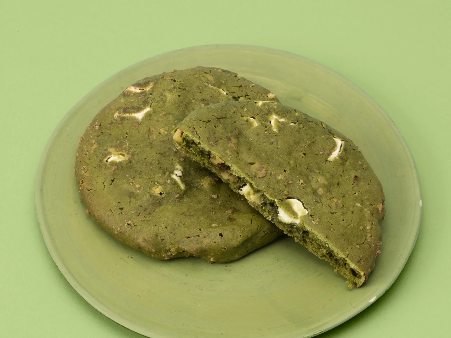 抹茶クッキーが緑色の皿に2つ並べられ、そのうち1つは半分に割られている写真です。