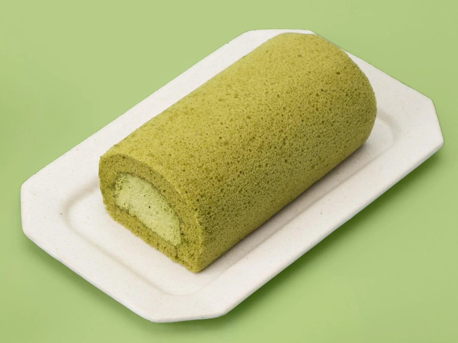 抹茶ロールケーキが白い長方形のお皿に載せられています。背景は黄緑色です。