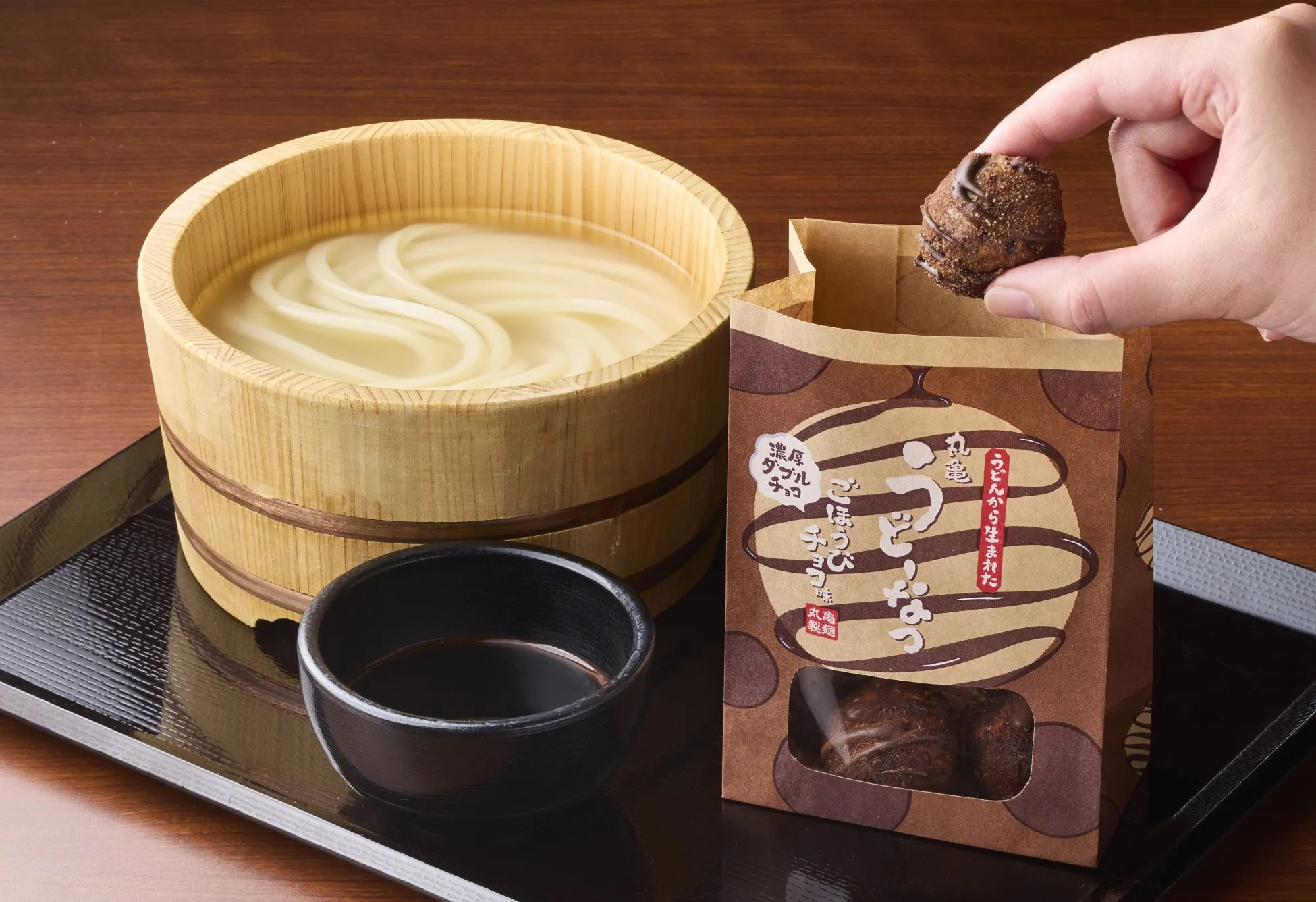 うどん、チョコレート、手で持っているチョコレート、木製の容器、木製のテーブルに置かれた黒いお盆