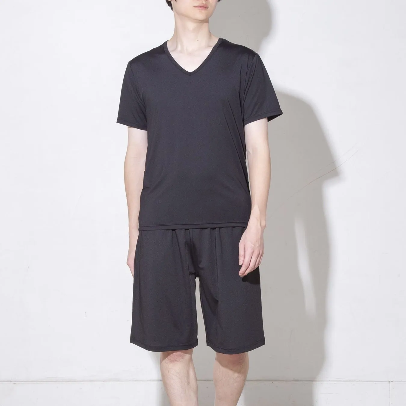 黒いVネックのTシャツと黒いハーフパンツを着用した男性が立っている写真です。