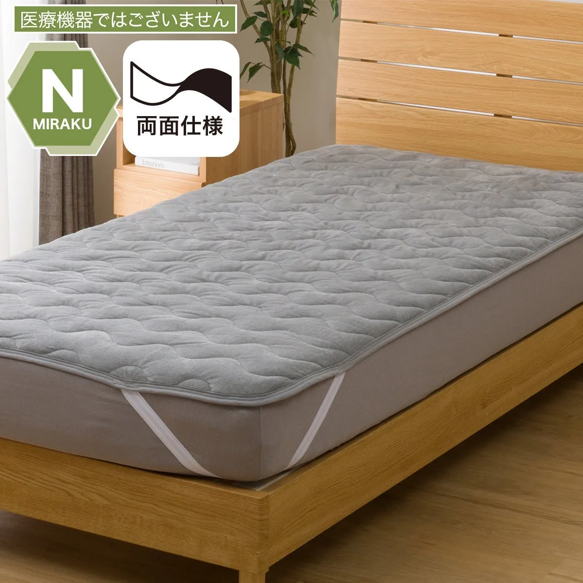 ベッドに敷かれたグレーのキルティング加工されたマットレス。白いゴムバンドで固定されている。木製のベッドフレーム。