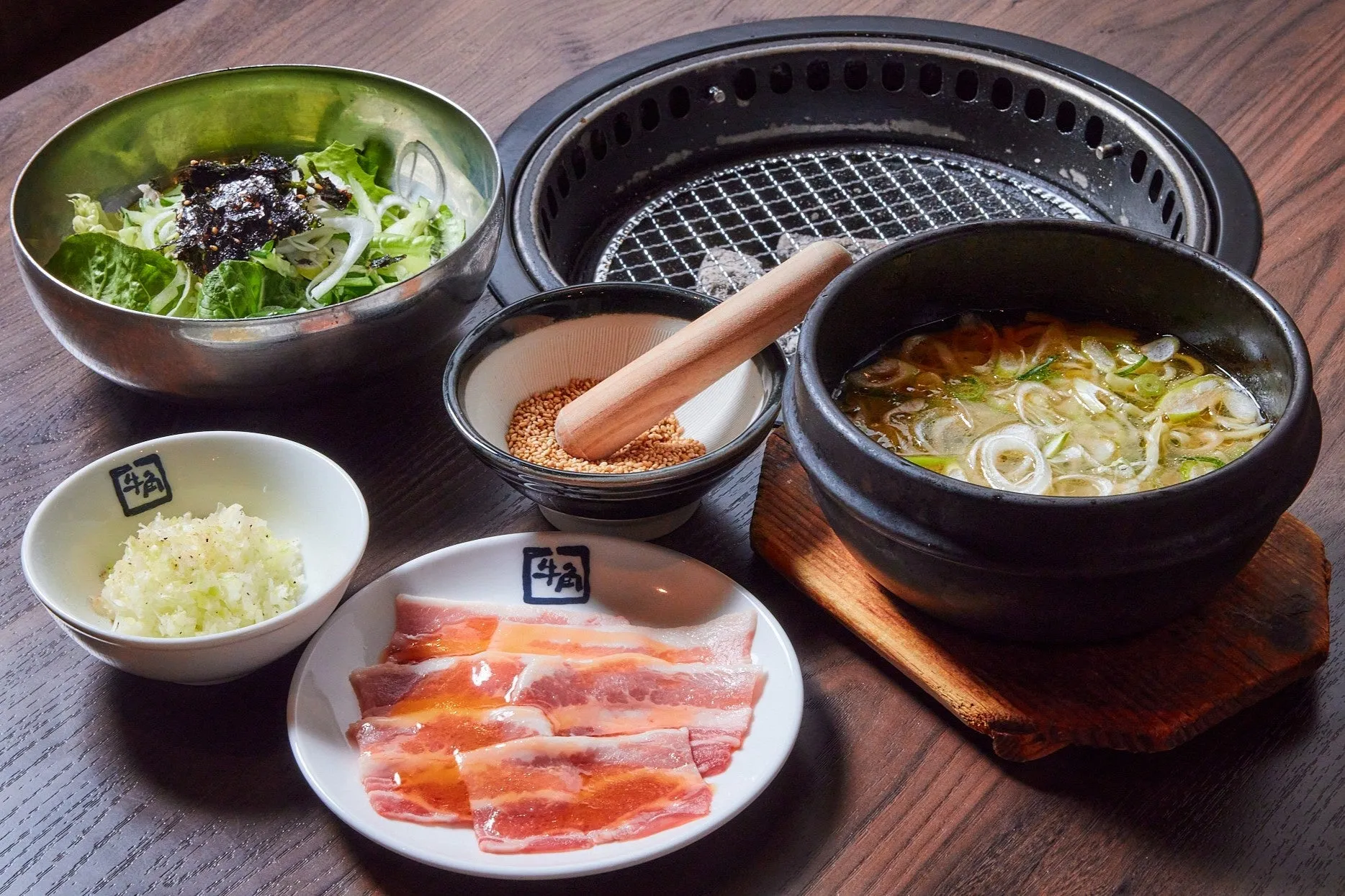 焼肉店のセットメニューの料理の写真です。サラダ、スープ、肉、薬味、ごま、焼き網などが見えます。