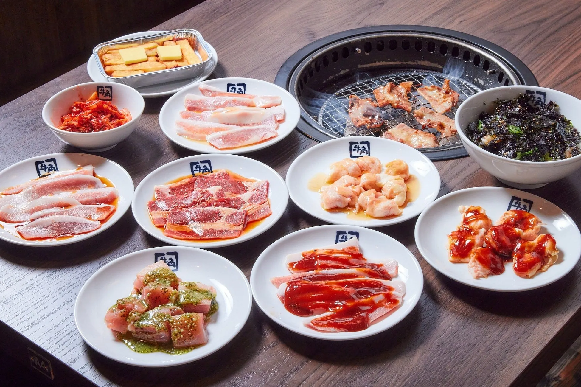 焼肉のセットの俯瞰写真。様々な種類の肉、キムチ、海苔ご飯などが並び、中央には焼肉用のコンロがある。