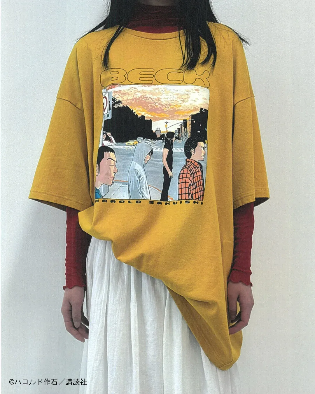 黄色いTシャツを着た女性。Tシャツには漫画「BECK」のイラストがプリントされており、重ね着をしている。