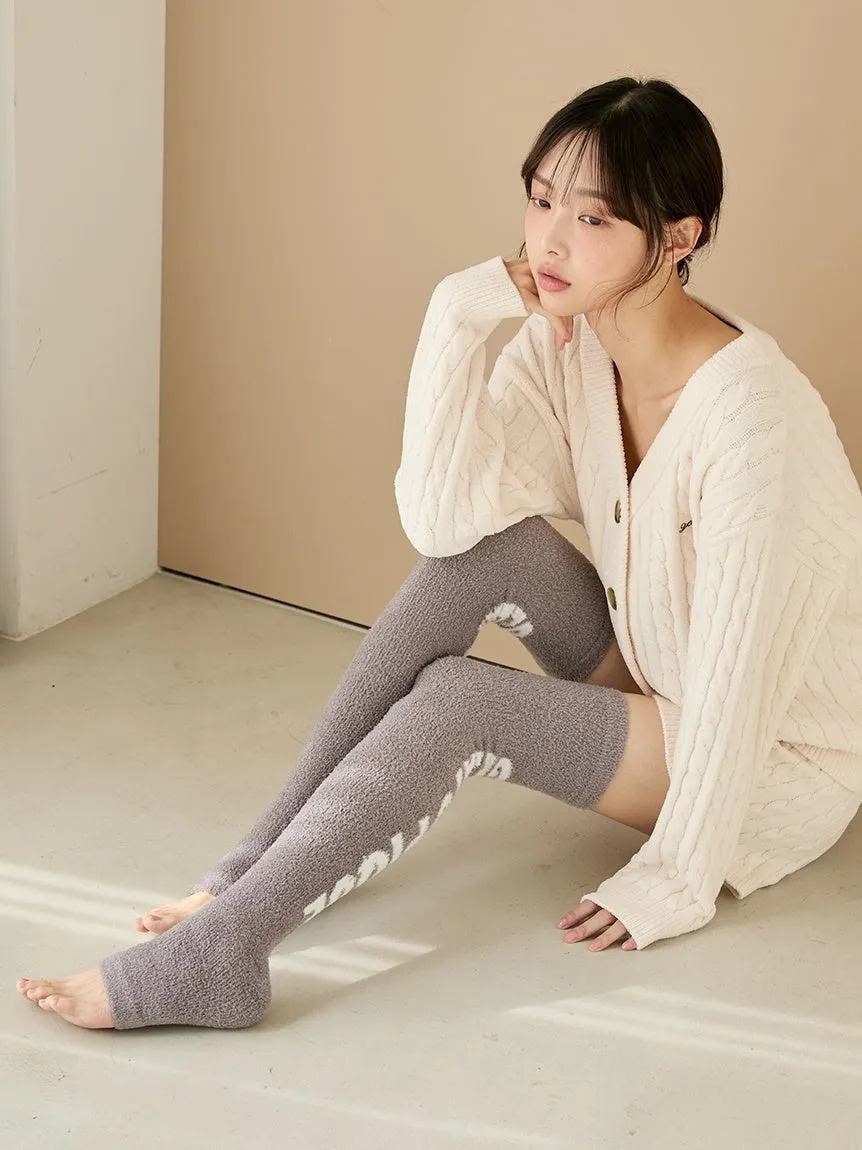 女性が床に座り、膝丈の靴下とカーディガンを着ている写真です。