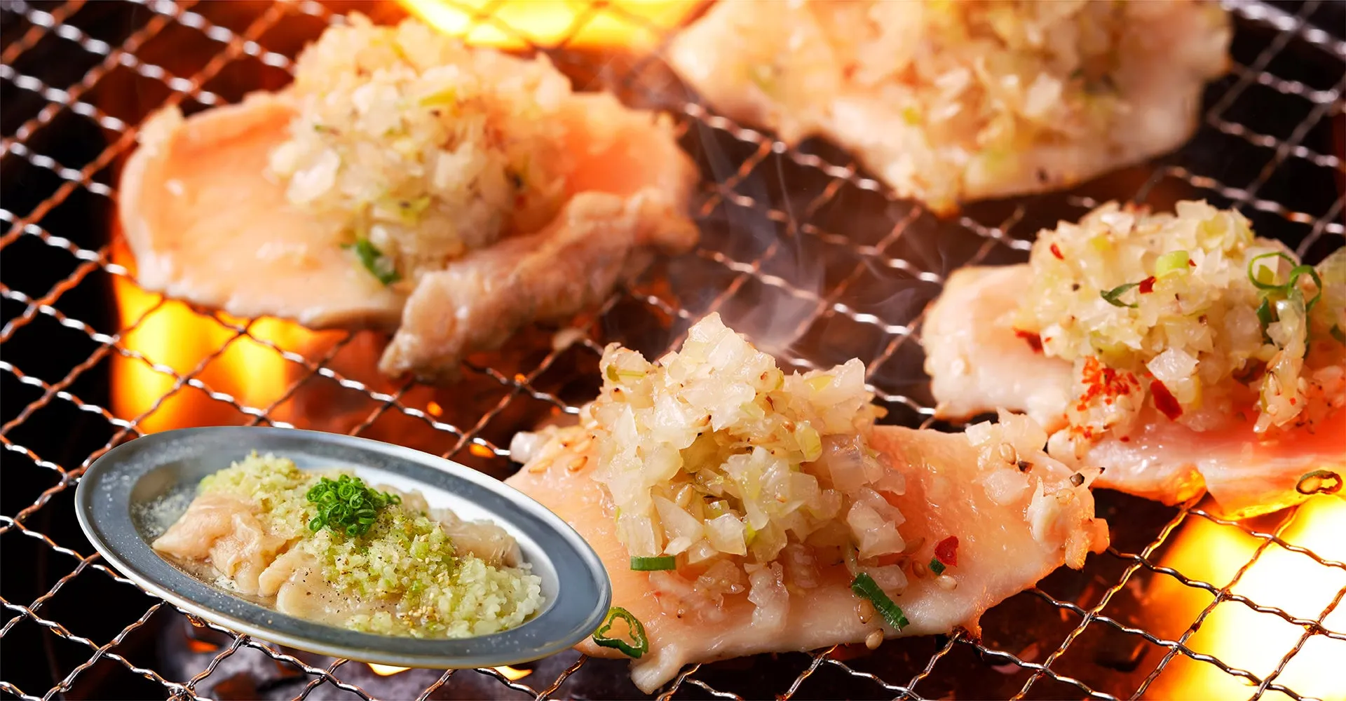 網の上で焼かれた鶏肉と、薬味を添えた鶏肉のアップ