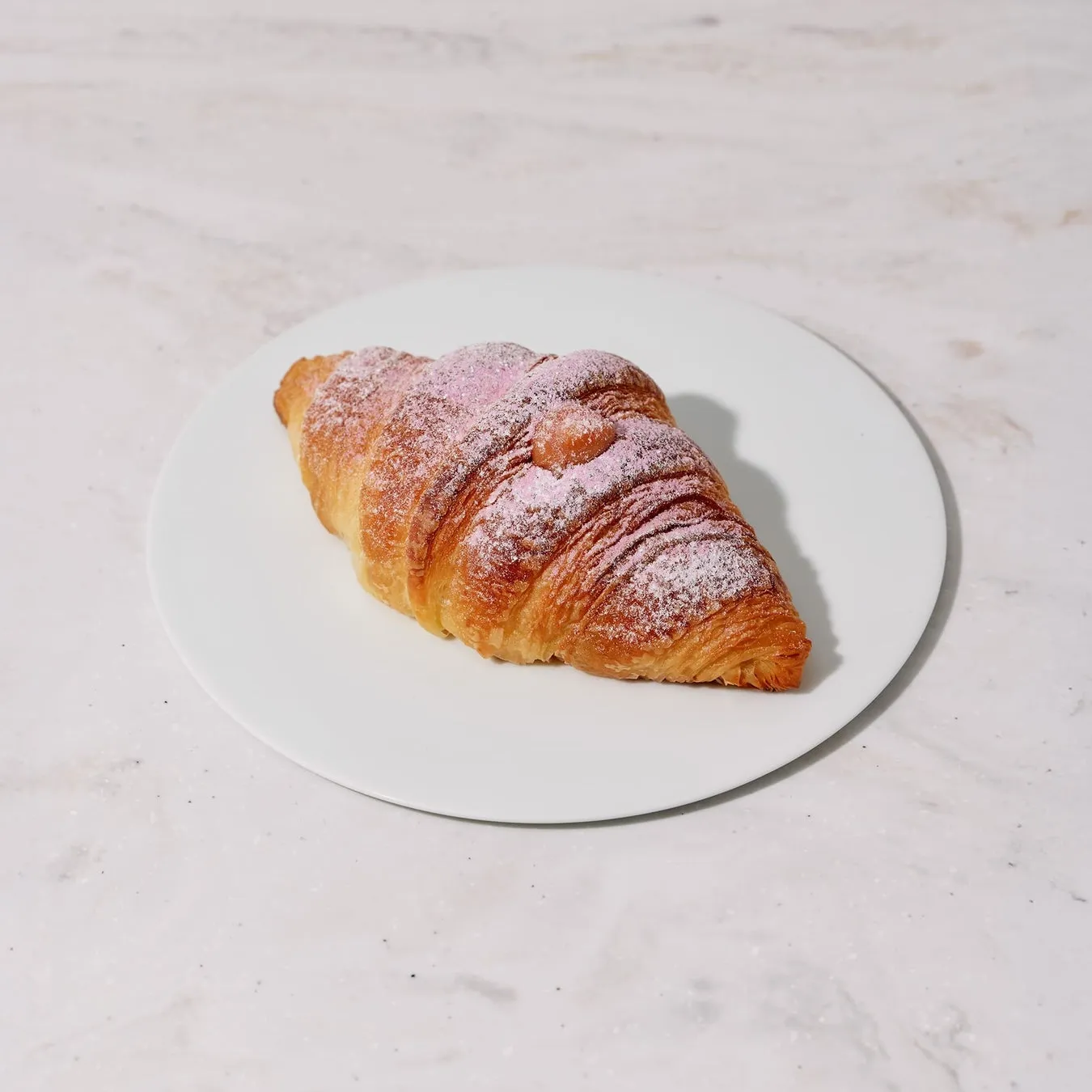 白い皿に載ったクロワッサン。粉砂糖とピンクのパウダーがまぶされている。