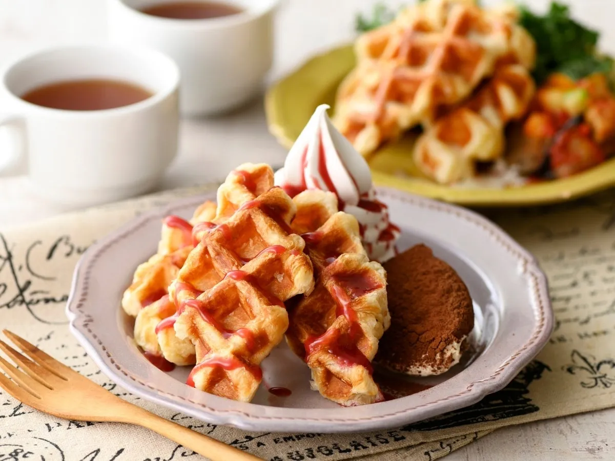 ワッフルとデザートが載ったお皿と、2つのカップに入った飲み物、フォークが写った写真