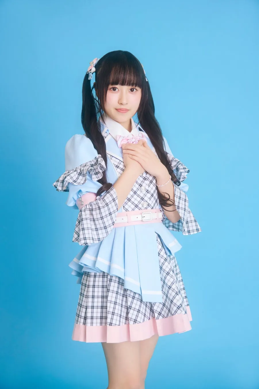 水色の背景に、アイドル風の衣装を着た女性が微笑んでいる写真。両手を胸の前で組んでおり、可愛らしいポーズをとっている。