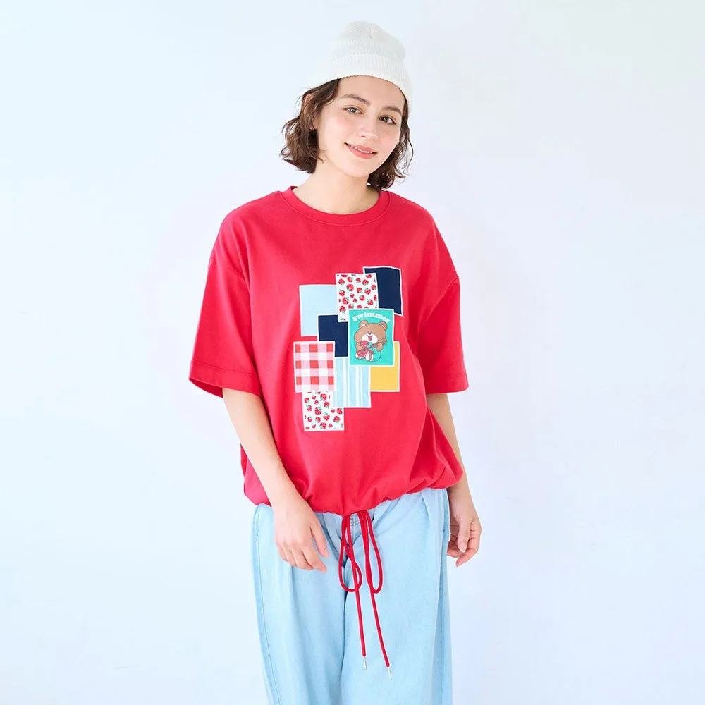赤いTシャツを着た女性の画像。Tシャツには、クマのイラストと「SWIMMER」の文字がプリントされた正方形の模様が施されている。女性は白い帽子をかぶり、水色のズボンを履いている。