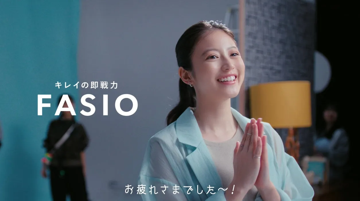 FASIOの広告画像。笑顔の女性が両手を合わせており、背景にはスタジオらしきセットが見える。