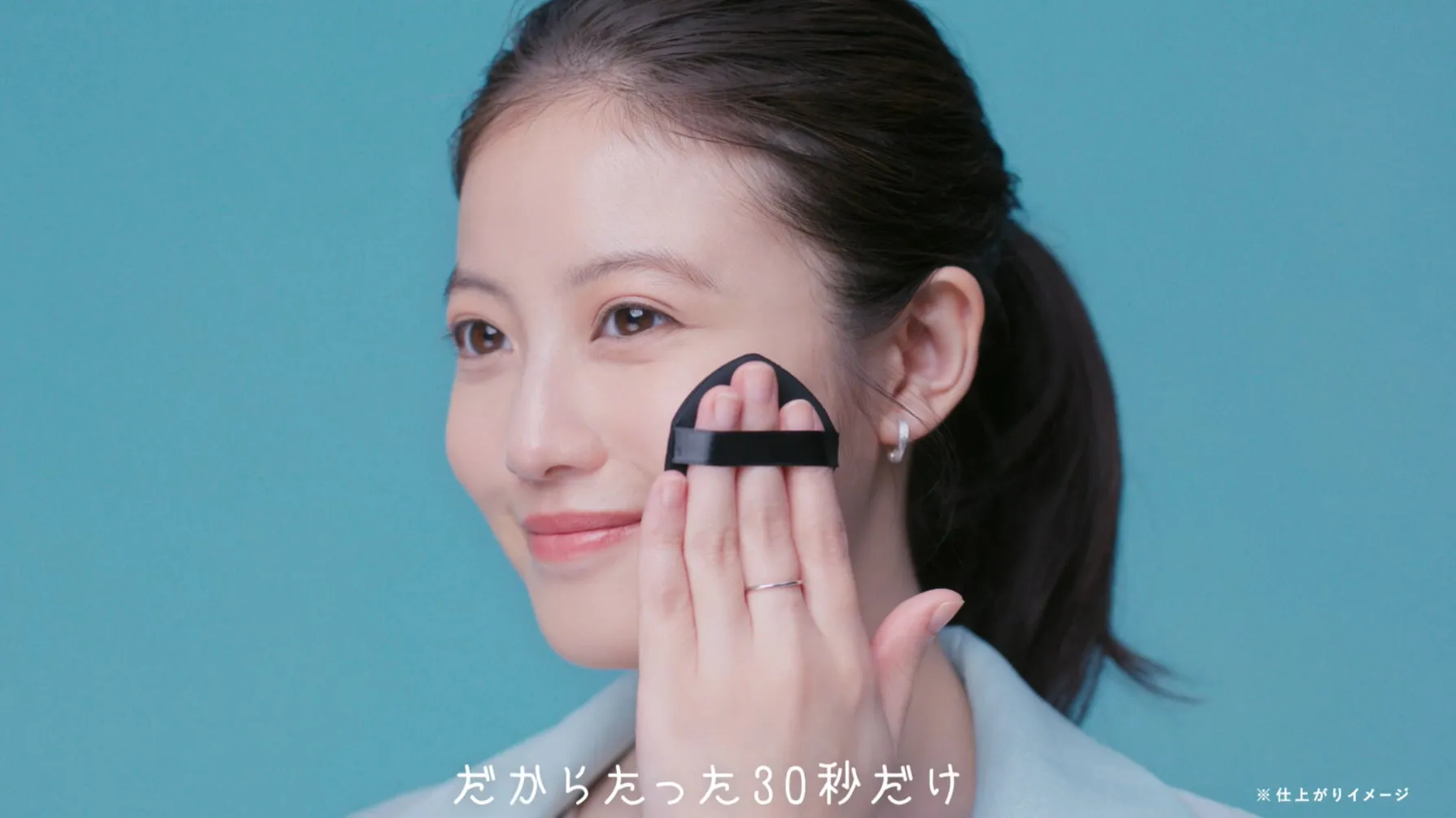 女性がパフを使って顔に化粧品を塗っている様子を写した広告画像です。