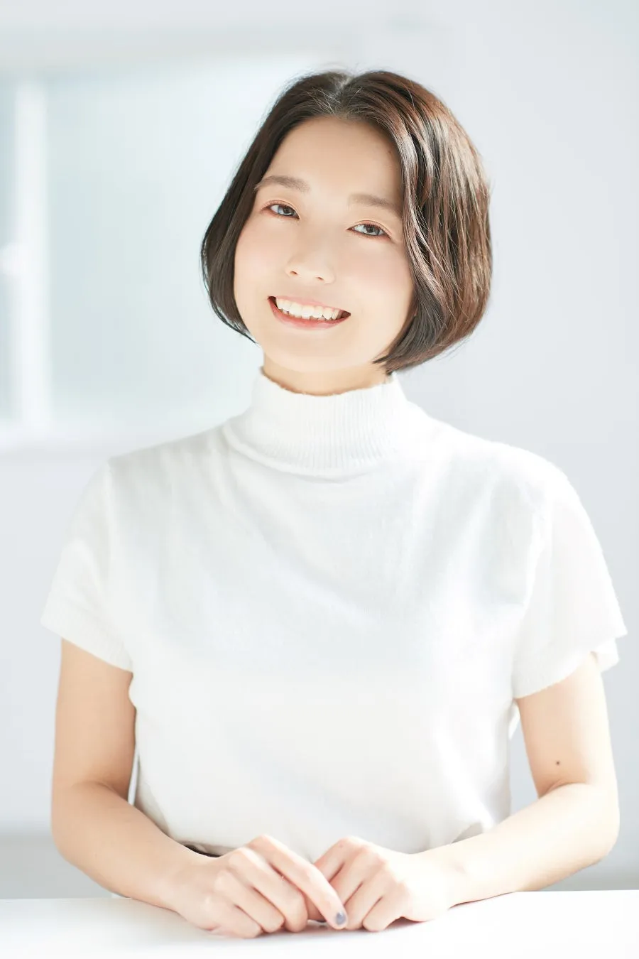 白いタートルネックのセーターを着て、テーブルに手を置いた女性のポートレート。