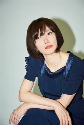 女性が座ってカメラの方を見ているポートレート写真。彼女は濃い色のドレスを着ており、短い茶色の髪と赤い唇をしている。