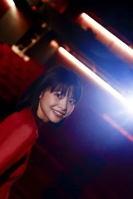 赤い服を着た女性が微笑んでいる写真。背景にはライトと赤い装飾がある。