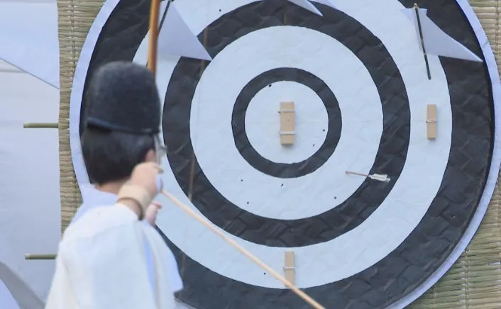 弓を射る人物と的が写った写真。的は白と黒の同心円で構成され、矢が刺さっている。人物は弓を構え、的を狙っている。