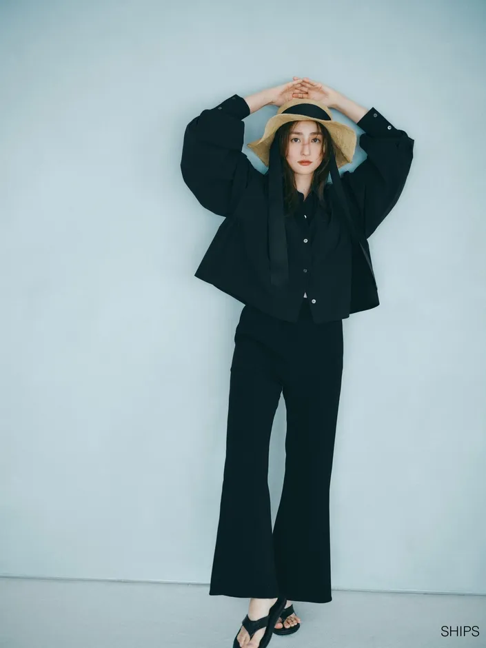 女性が黒い服を着て、麦わら帽子をかぶり、ポーズをとっています。