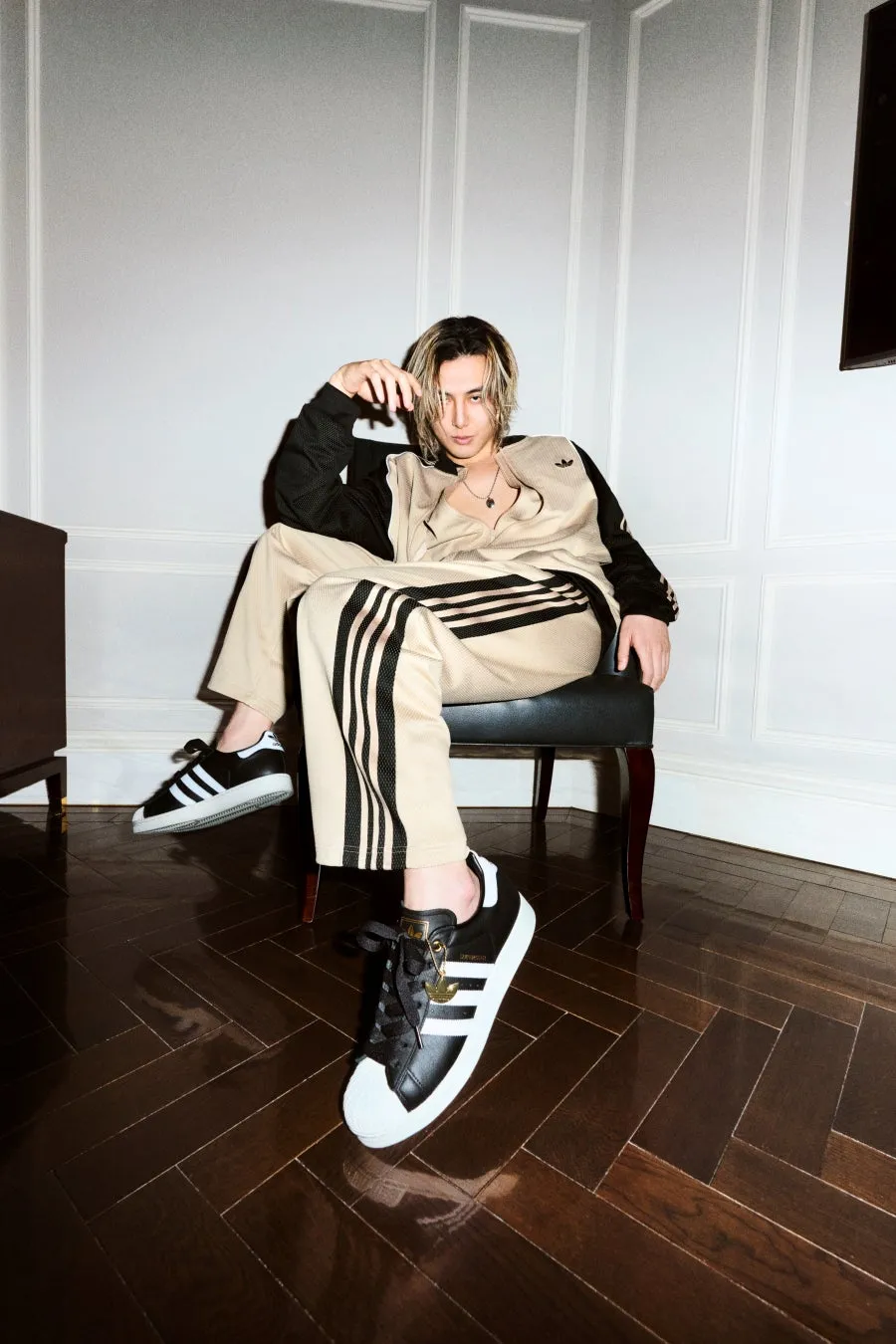 アディダスのトラックスーツを着た男性が椅子に座ってポーズをとっている写真です。