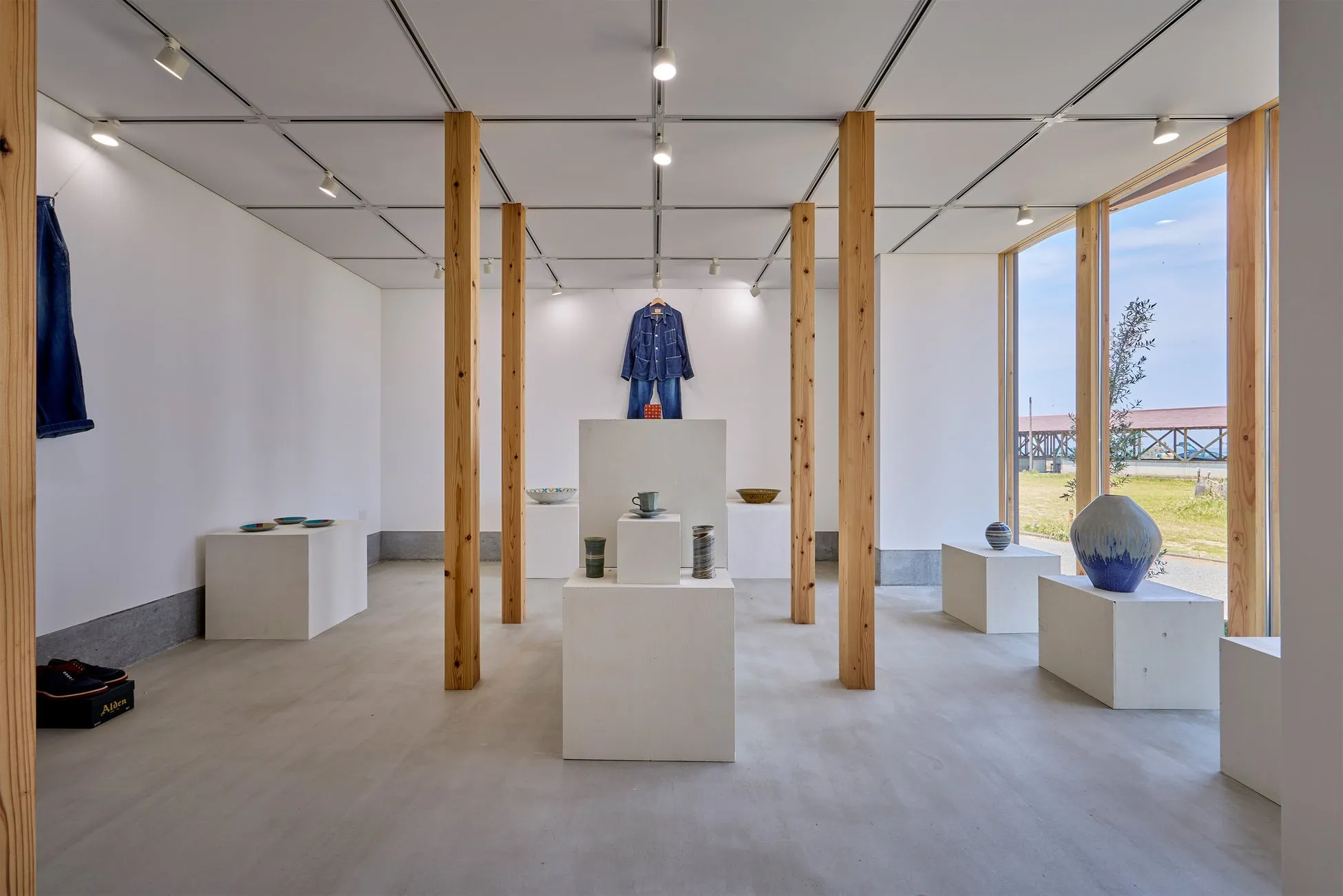 白い壁と木製の柱のある展示室。中央にはデニムのジャケットとズボンが展示