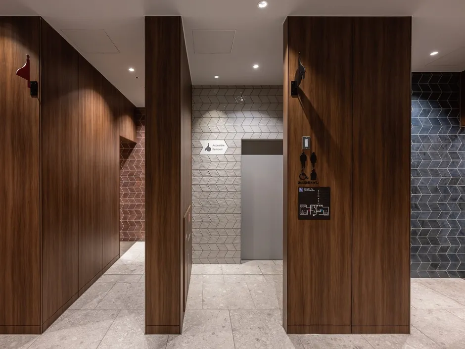 木製の壁と床が特徴的な、ホテルの廊下の内観写真。廊下には、トイレの入り口を示す案内板や、点字表記の案内板が設置されている。