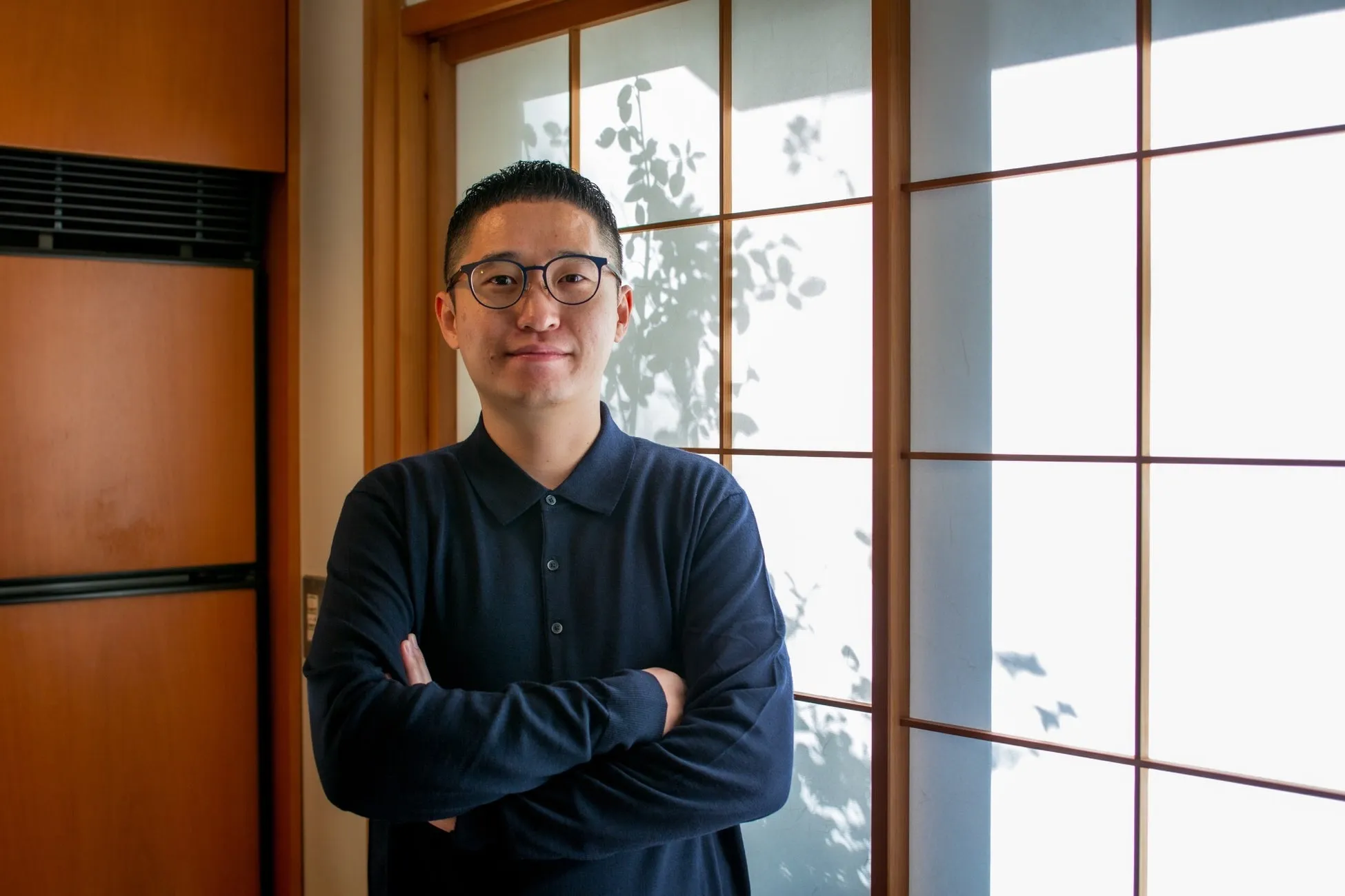 眼鏡をかけた男性が腕を組んで立っている写真