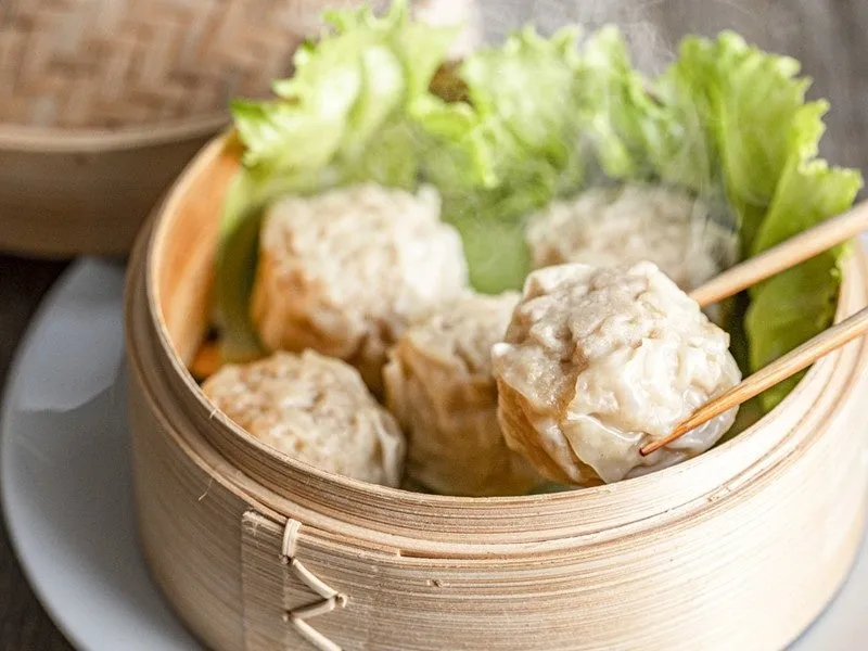 蒸籠に入った焼売。箸で焼売をつまんでいる。