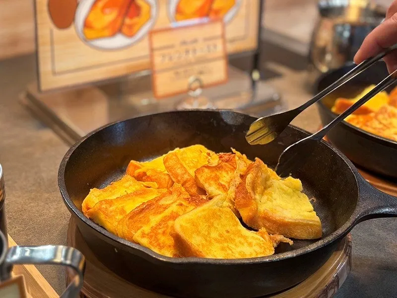 鉄板に盛られたフレンチトーストの写真です。トングで取り分けようとしている様子です。