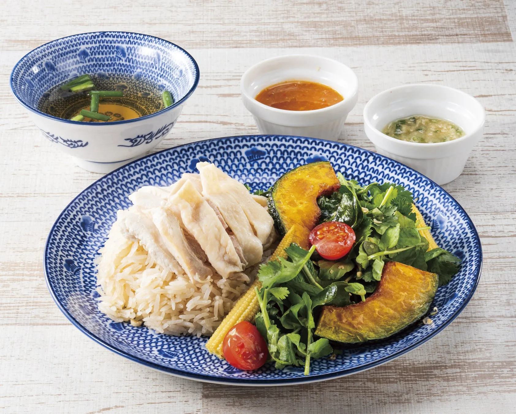 白い器に入ったスープ、ソース、鶏肉とご飯、野菜が盛り付けられた料理の写真です。