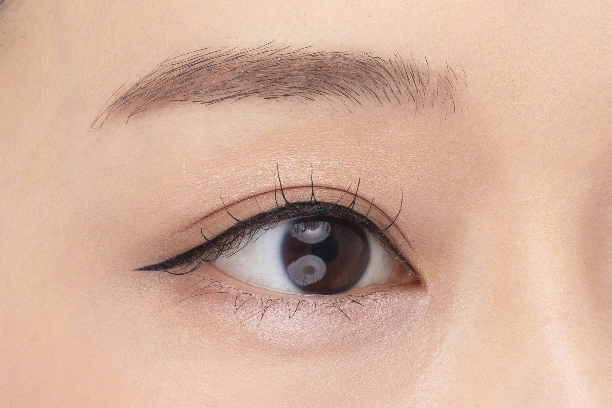 目のクローズアップ。アイライナーとマスカラが施されています。まぶたには軽いアイシャドウが塗られています。眉毛は整えられています。