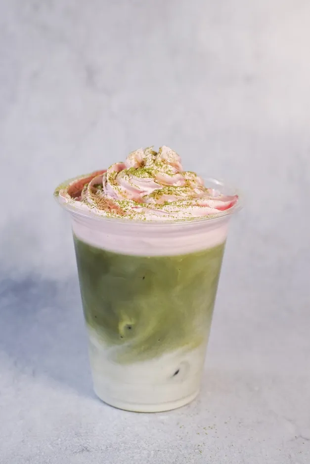 抹茶ラテの上にピンク色のクリームと抹茶パウダーがトッピングされた飲み物