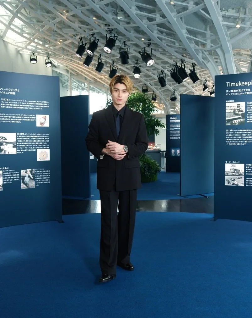 男性がスーツを着て、展示会場に立っている写真。背景には時計の歴史に関する展示物がある。