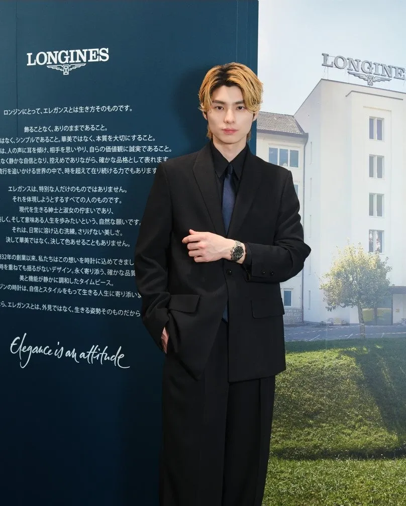 ロンジンの時計を身につけた男性の広告画像。背景にはロンジンのロゴと建物が写っている。男性は黒いスーツを着ており、時計がよく見えるように手首を前に出している。画像には「Elegance is an attitude」という文字も含まれている。
