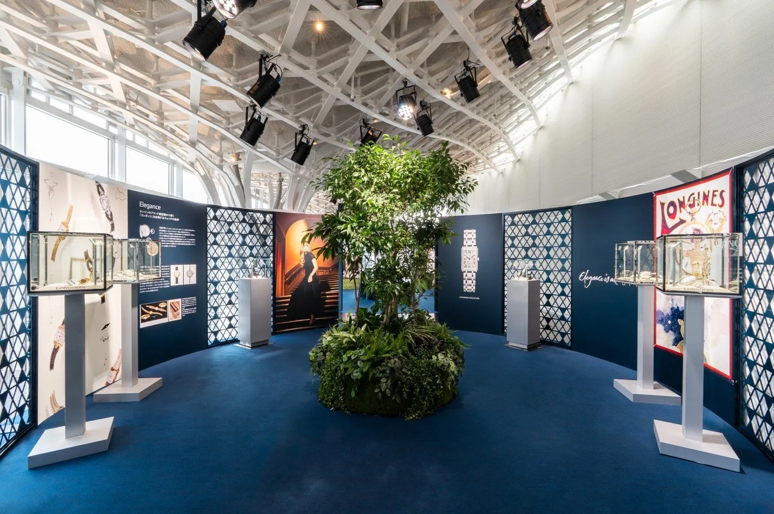 ロンジン時計のエレガンスをテーマにした展示会。中央には木が置かれ、青いカーペットと白い天井が特徴的。
